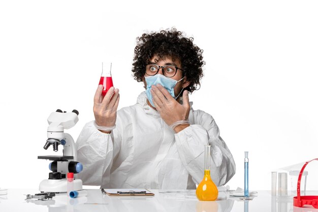 Front view male doctor in protective suit and mask holding flask with red solution on white desk pandemic covid epidemic virus