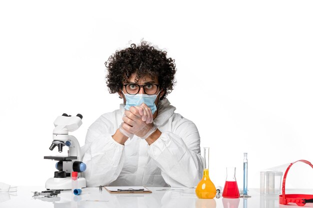 Front view male doctor in protective suit and mask just sitting with solutions on white