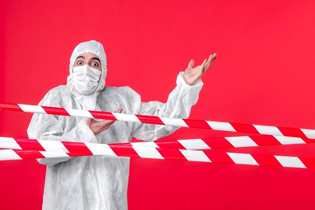 Front view male doctor in protective suit and mask on red background health cure hospital covid- quarantine color isolation