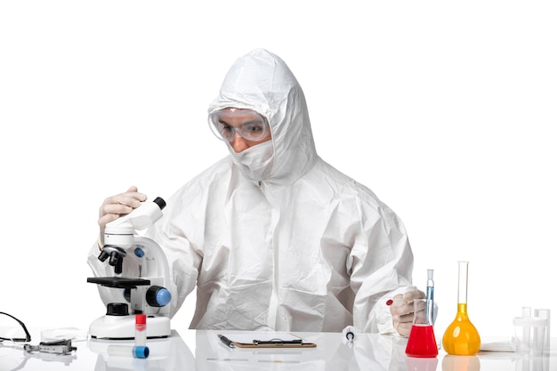 Front view male doctor in protective suit with mask due to covid holding flask on white desk