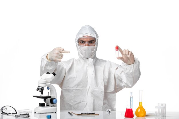 Front view male doctor in protective suit with mask due to covid holding flask on the white space