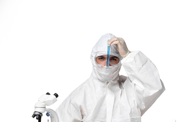 Front view male doctor in protective suit with mask due to covid holding flask with blue solution on a white space