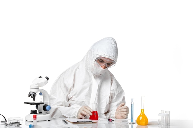 Front view male doctor in protective suit with mask due to covid holding flask with red solution on a white space