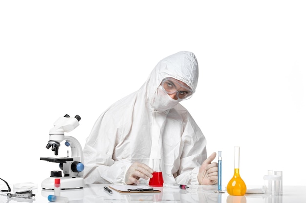 Front view male doctor in protective suit with mask due to covid holding flask with red solution on white space