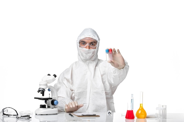 Front view male doctor in protective suit with mask due to covid holding flasks on white desk