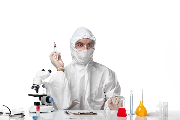 Вид спереди мужчина-врач в защитном костюме с маской из-за covid, держащего инъекцию на белом пространстве