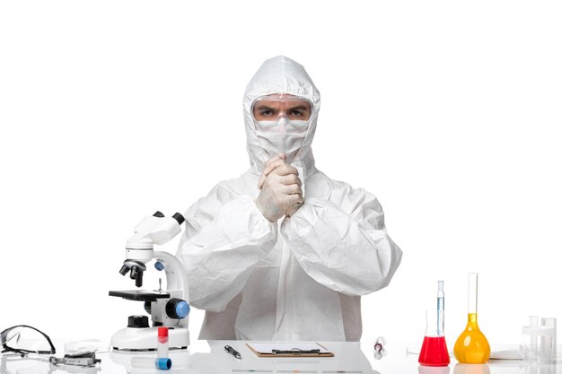 Front view male doctor in protective suit with mask due to covid just sitting on white desk