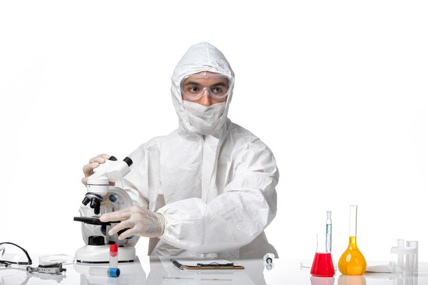 明るい白いスペースで顕微鏡を使用してcovidのためにマスクと防護服を着た正面図の男性医師