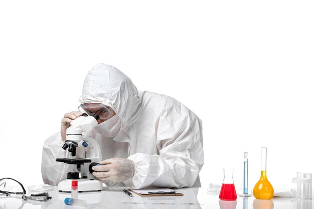 Front view male doctor in protective suit with mask due to covid using microscope on white space