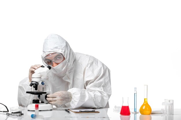 Front view male doctor in protective suit with mask due to covid using microscope on white space