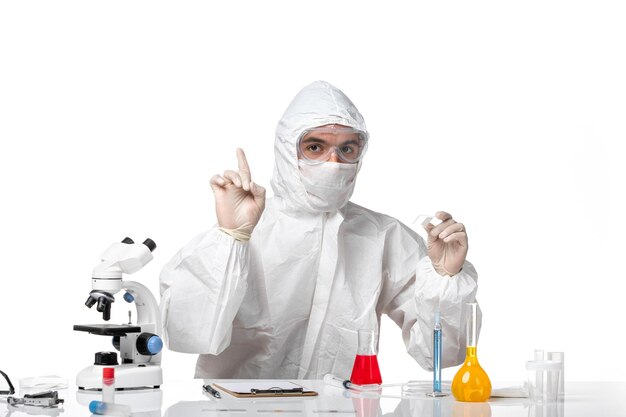白い机の上のソリューションでcovid作業のため、マスク付きの防護服を着た正面図の男性医師