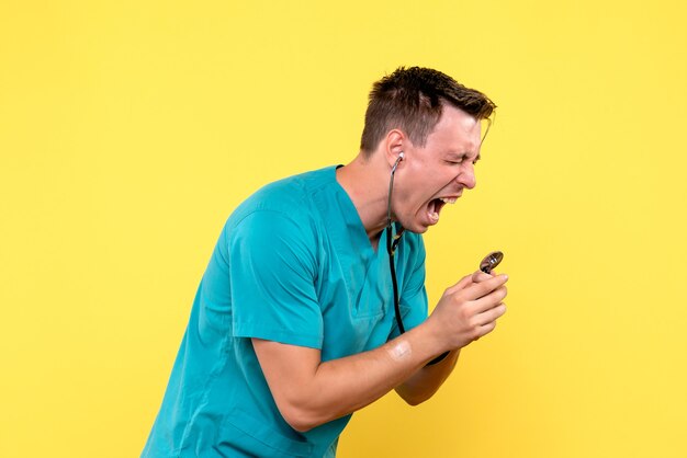 Вид спереди мужского врача, кричащего на тонометре на желтой стене