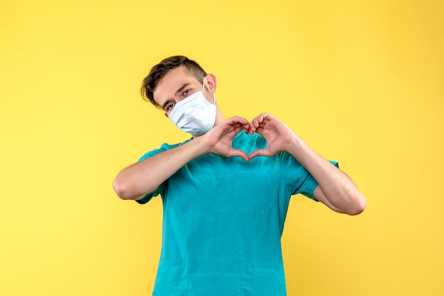 Front view of male doctor sending love in mask on yellow wall