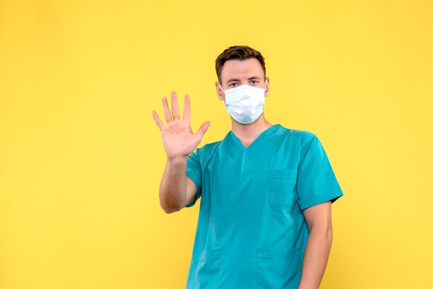 Front view of male doctor showing his palm on yellow wall