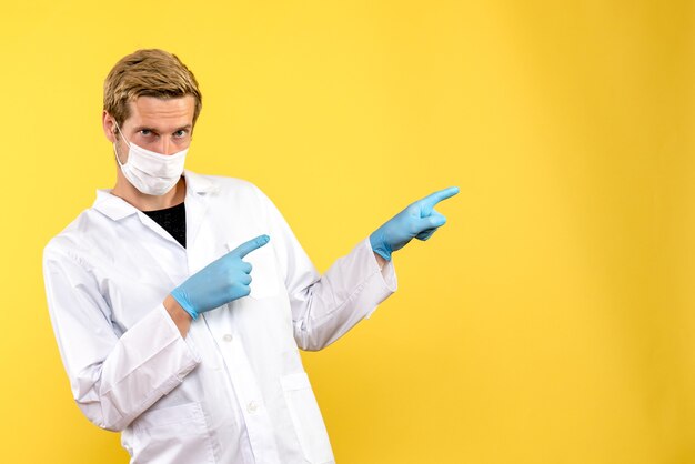 Front view male doctor in sterile mask on yellow background covid- pandemic health medic