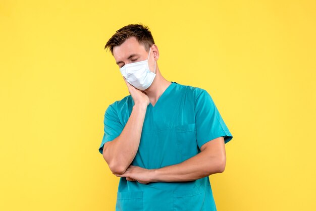 Front view of male doctor in sterile mask on a yellow wall