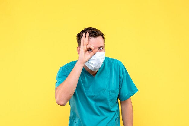 Front view of male doctor in sterile mask on a yellow wall