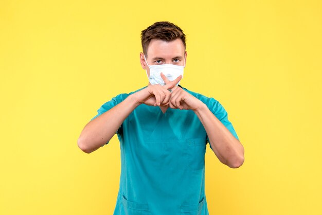 Front view of male doctor in sterile mask on yellow wall