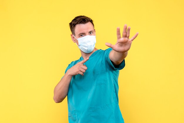 Front view of male doctor in sterile mask on yellow wall