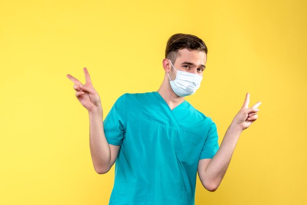 Front view of male doctor in sterile mask on yellow wall