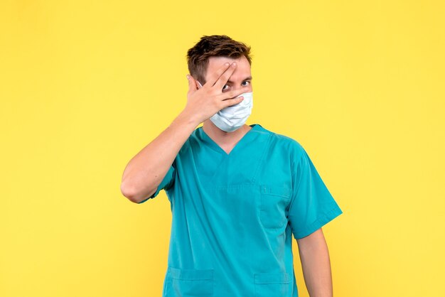 Вид спереди мужского врача в стерильной маске на желтой стене
