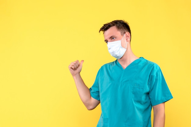 Вид спереди мужского врача в стерильной маске на желтой стене