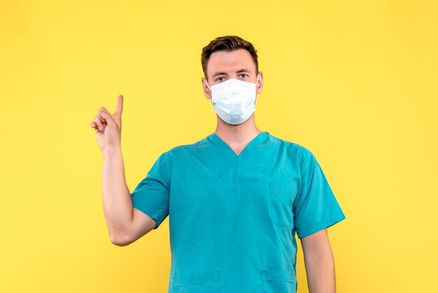 Front view of male doctor in sterile mask on yellow wall