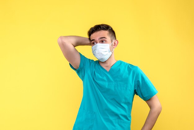 Front view of male doctor in sterile mask on yellow wall