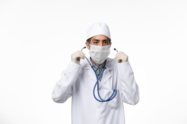 白い表面のコロナウイルスによる無菌医療スーツとマスクの正面図男性医師