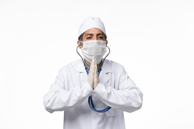 Front view male doctor in sterile medical suit and mask due to coronavirus on white surface