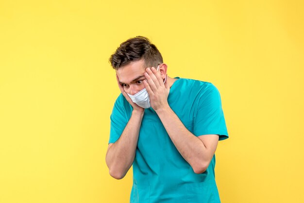 Front view of male doctor stressed in mask on a yellow wall