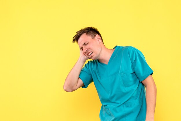 Front view of male doctor suffering from head pain on yellow wall