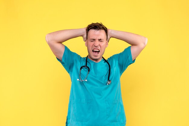 Front view of male doctor suffering from headache on yellow wall