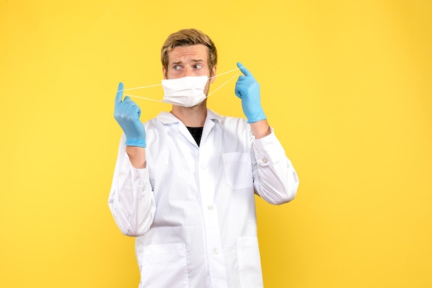 Front view male doctor taking off mask on yellow background pandemic covid health