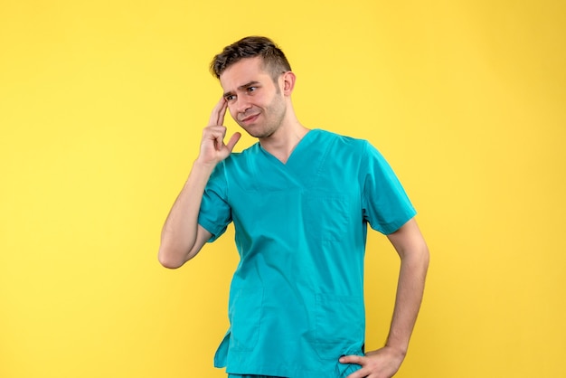 Front view of male doctor thinking on yellow wall