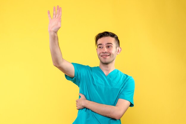 黄色の壁に手を振っている男性医師の正面図
