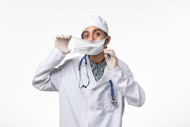 明るい白い表面にマスクを着用しているコロナウイルスによる白い医療スーツの正面図男性医師