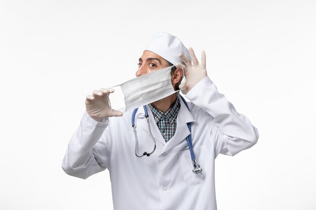 白い表面にマスクを着用しているコロナウイルスによる白い医療スーツの正面図男性医師