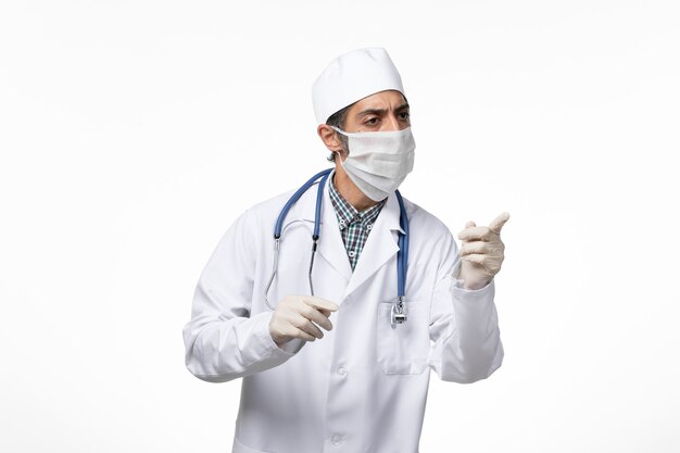 Front view male doctor in white medical suit and mask due to coronavirus on a white surface