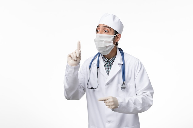 白い表面のコロナウイルスによる白い医療スーツとマスクの正面図男性医師