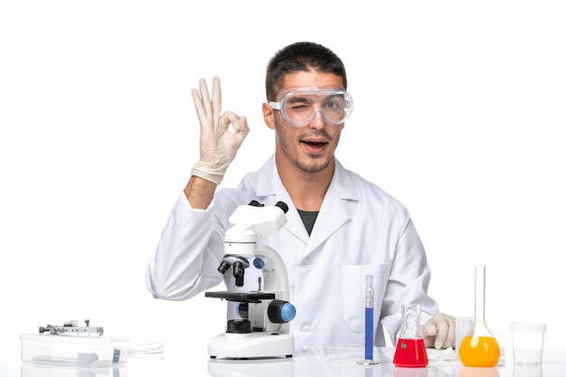 Front view male doctor in white medical suit sitting with solutions on light white space