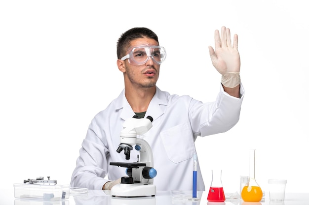 Front view male doctor in white medical suit sitting with solutions on white desk