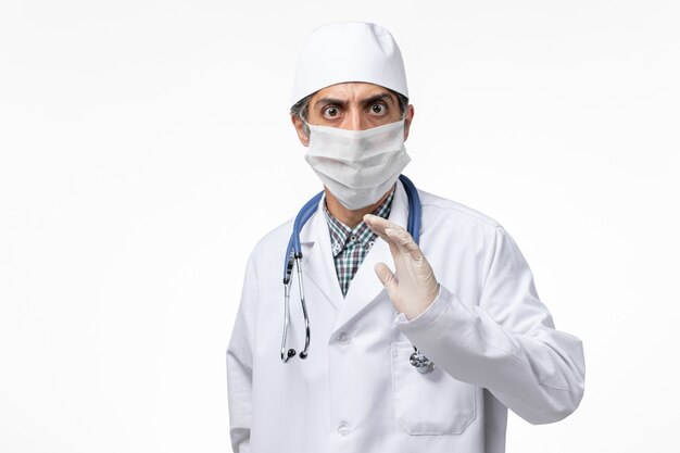 明るい白い机の上にcovidのためにマスクを身に着けている白い医療スーツの正面図男性医師