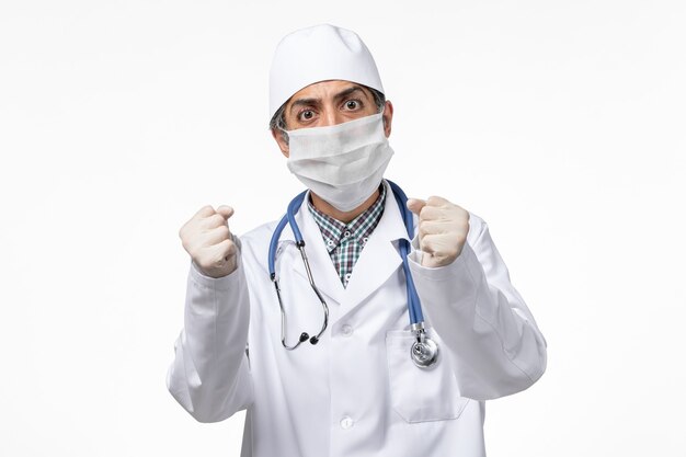 Front view male doctor in white medical suit wearing mask due to covid- on a white surface