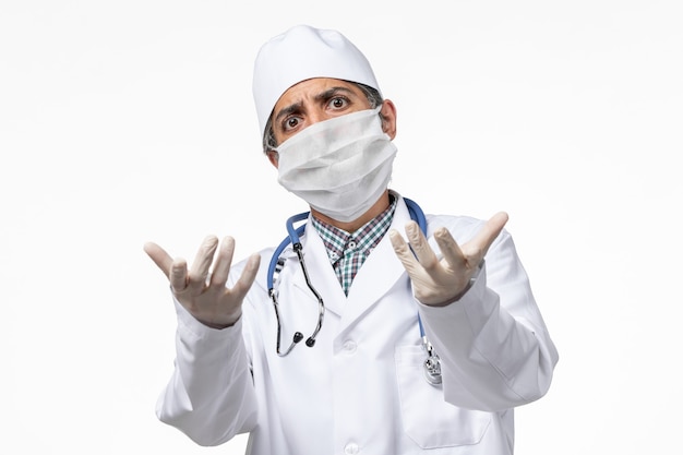白い表面にcovidのためにマスクを身に着けている白い医療スーツの正面図男性医師