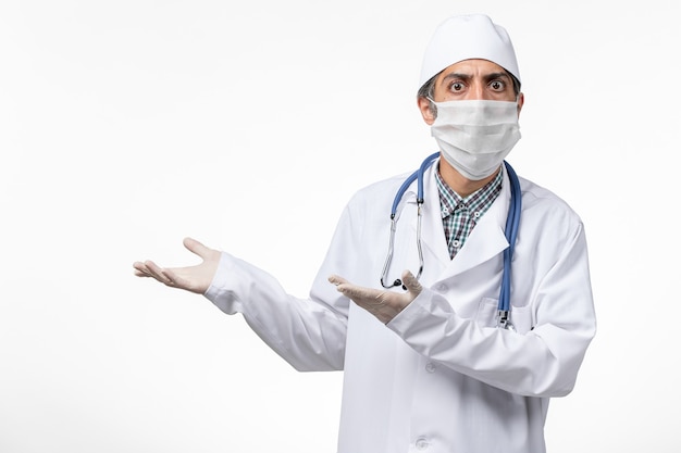 Front view male doctor in white medical suit wearing mask due to covid on white surface