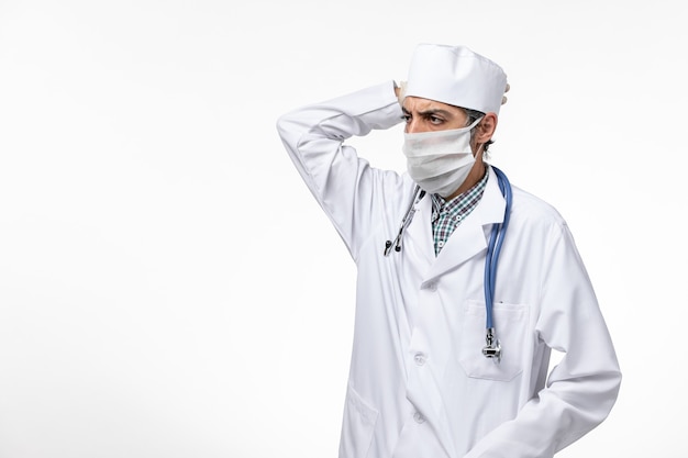 Medico maschio di vista frontale in tuta medica bianca con maschera a causa del pensiero del coronavirus sulla superficie bianca