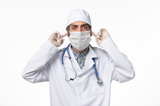 Вид спереди мужчина-врач в белом медицинском костюме с маской из-за коронавируса на белой поверхности