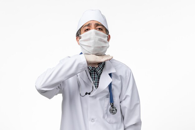 明るい白い表面にcovidのため、マスク付きの白い医療スーツの正面図男性医師