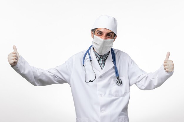 Вид спереди мужчина-врач в белом медицинском костюме с маской из-за ликования covid на белой поверхности